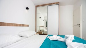 Ett hotellrum med en säng, ett turkosfärgat sängöverkast, vita kuddar, ett träfärgat sänggavel, en skjutdörr och ett nattduksbord med en lampa.