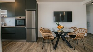A modern kitchen with dark cabinetry, a stainless steel refrigerator, a built-in oven, and a dining area with wicker chairs and a glass table. - Spacious Luxury Trogir Apartments (Trogir)