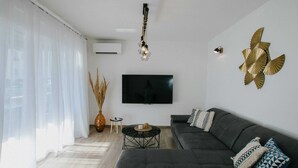 A modern living room with a dark grey sofa, a flat-screen TV, a decorative wall piece, and a hanging light fixture. - Spacious Luxury Trogir Apartments (Trogir)