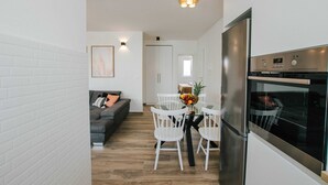 A modern kitchen with white cabinetry, a stainless steel oven, and a dining area with white chairs and a glass table. - Spacious Luxury Trogir Apartments (Trogir)