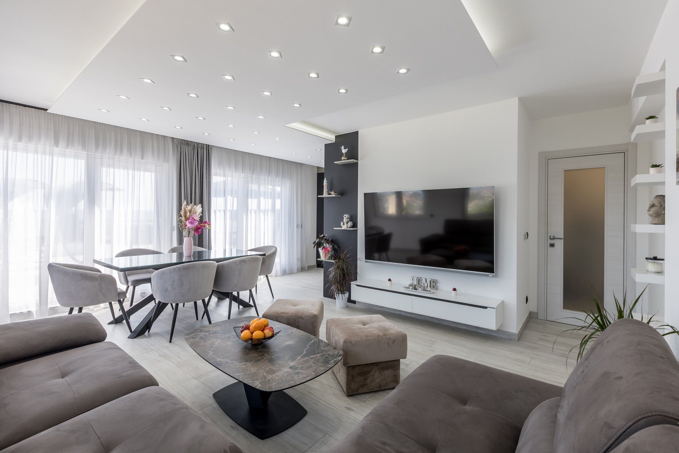 Een moderne woonkamer met een eethoek, een wandmontage flatscreen tv en een minimalistisch design.