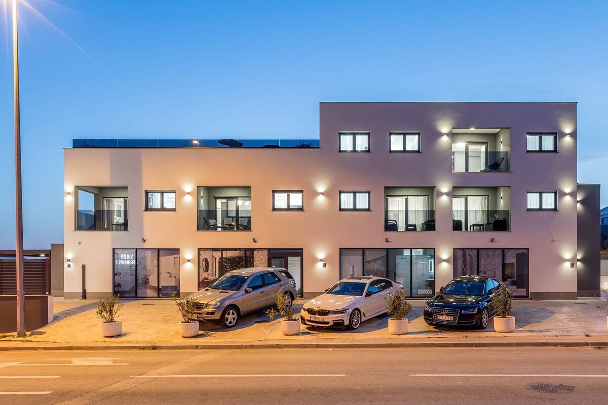 Un immeuble moderne à plusieurs étages, avec trois voitures garées devant.