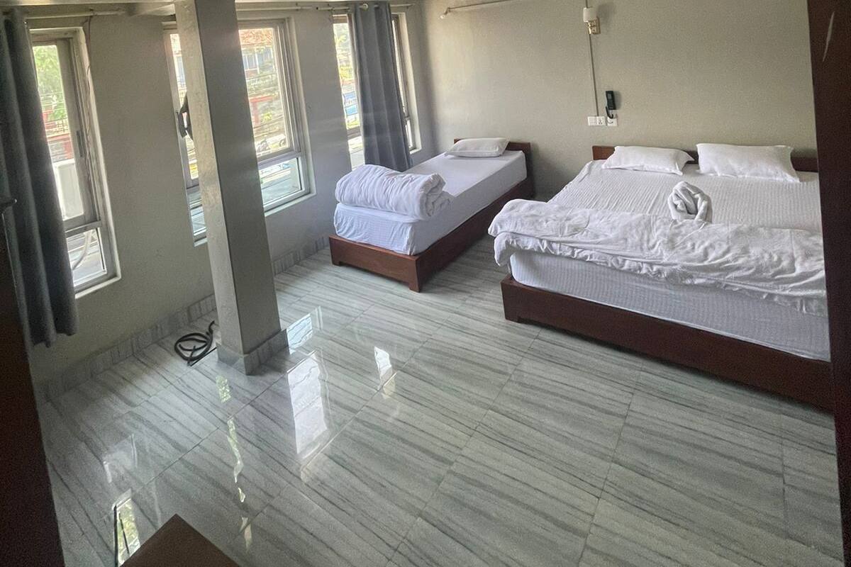 Une chambre d’hôtel avec deux lits, de grandes fenêtres et un sol carrelé.