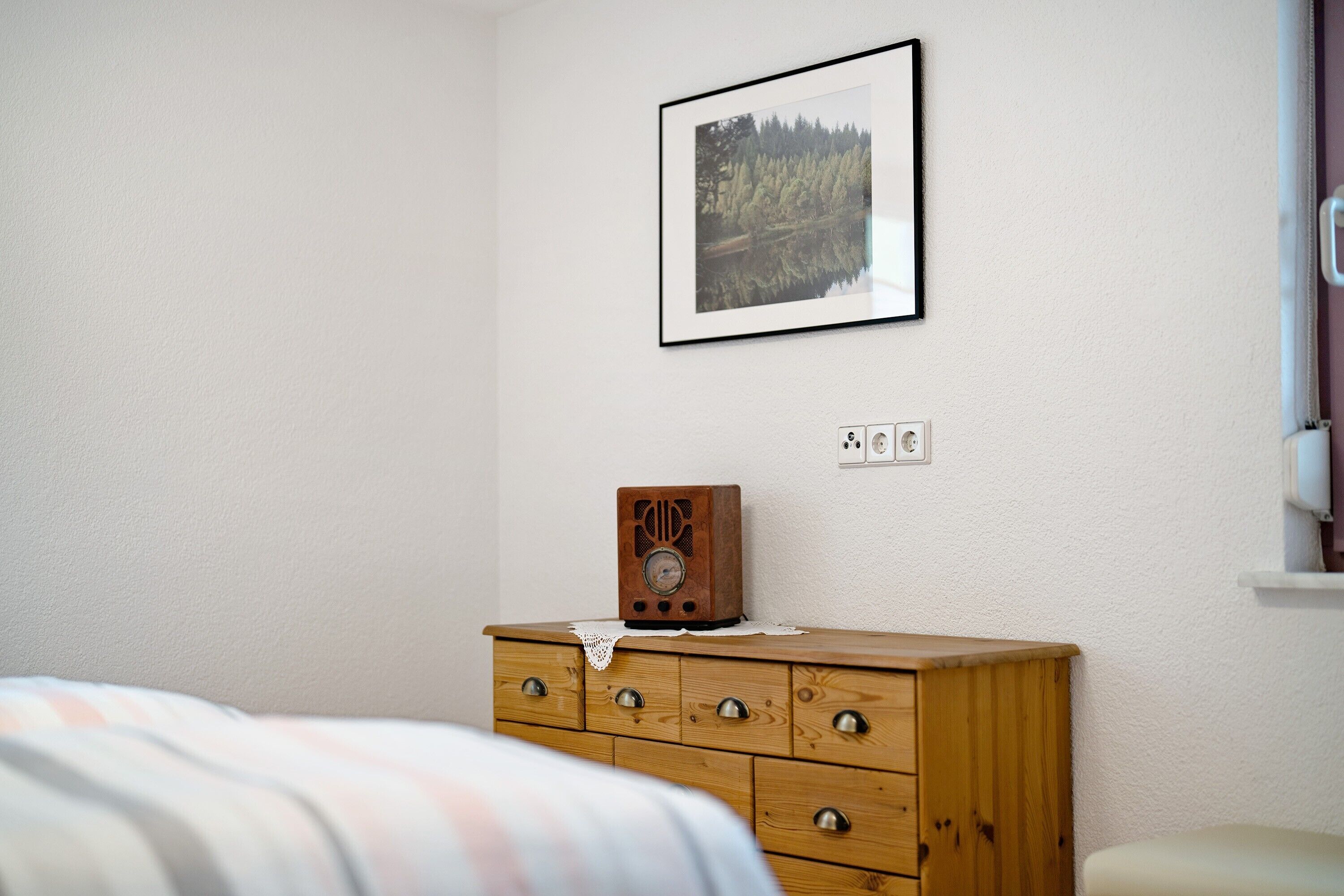Una camera da letto con un comò in legno, un quadro appeso alla parete e un letto con coperta a righe.