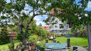 A garden with a metal table and chairs, potted plants, and a birdhouse.