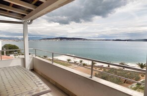 A balcony with a view of a calm sea and distant hills.
