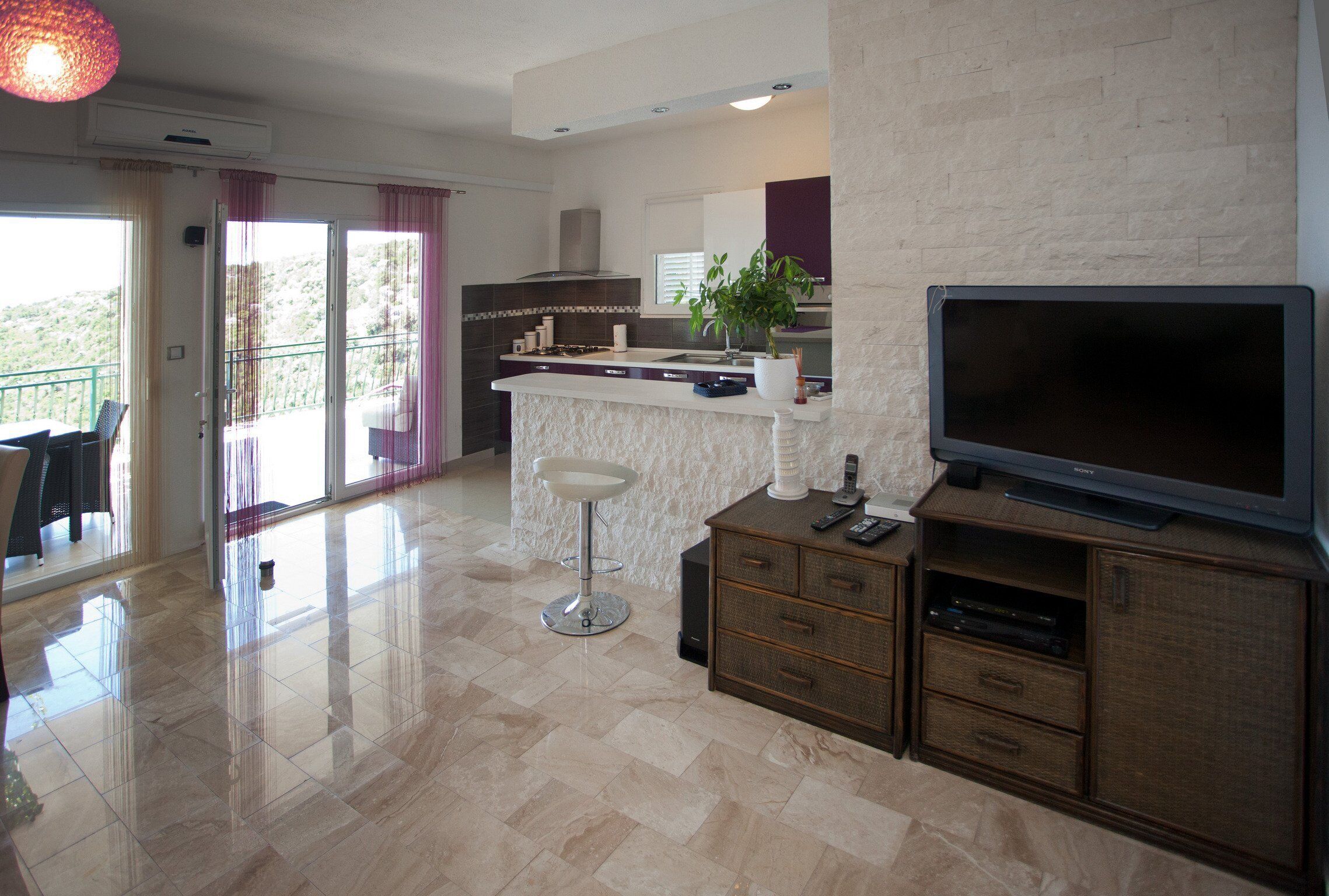 A modern kitchen with a large TV, a bar stool, and a dining area with a view.