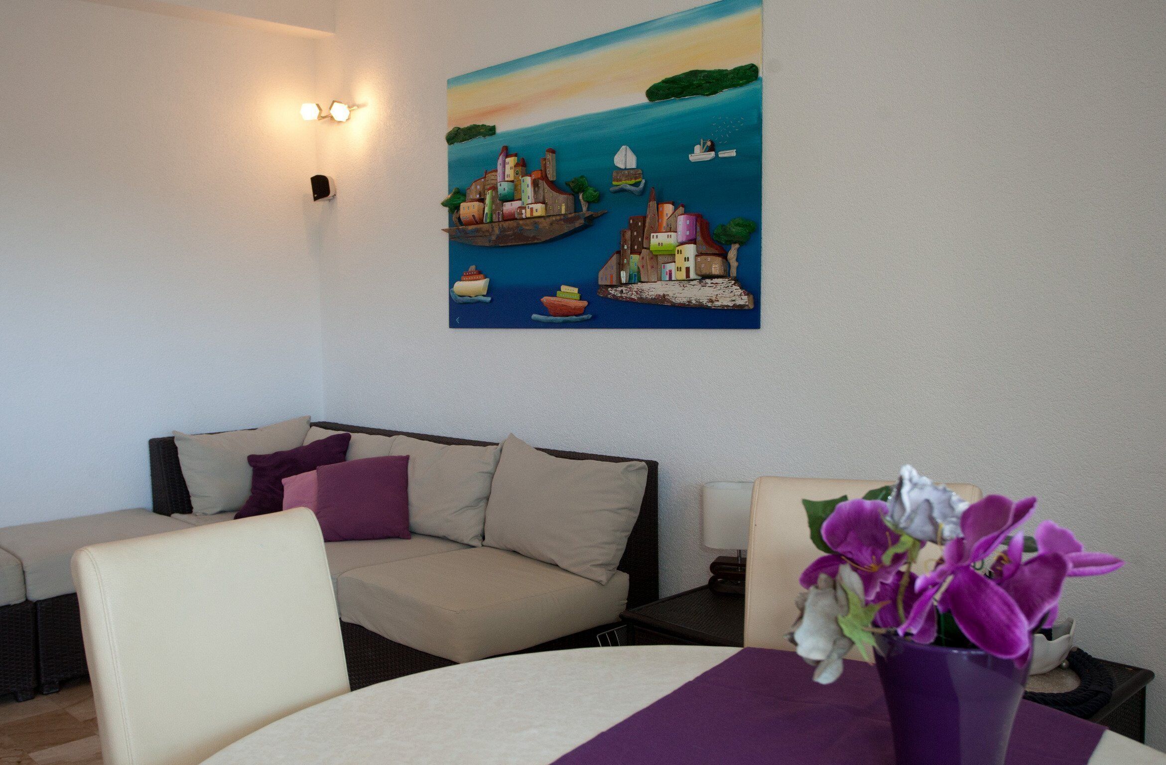 Ein Hotelzimmer mit einer Couch, einem Esstisch mit violettem Tischläufer und einem Gemälde einer Küstenlandschaft.