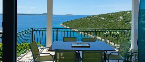A balcony with a table and chairs overlooking a coastal view.