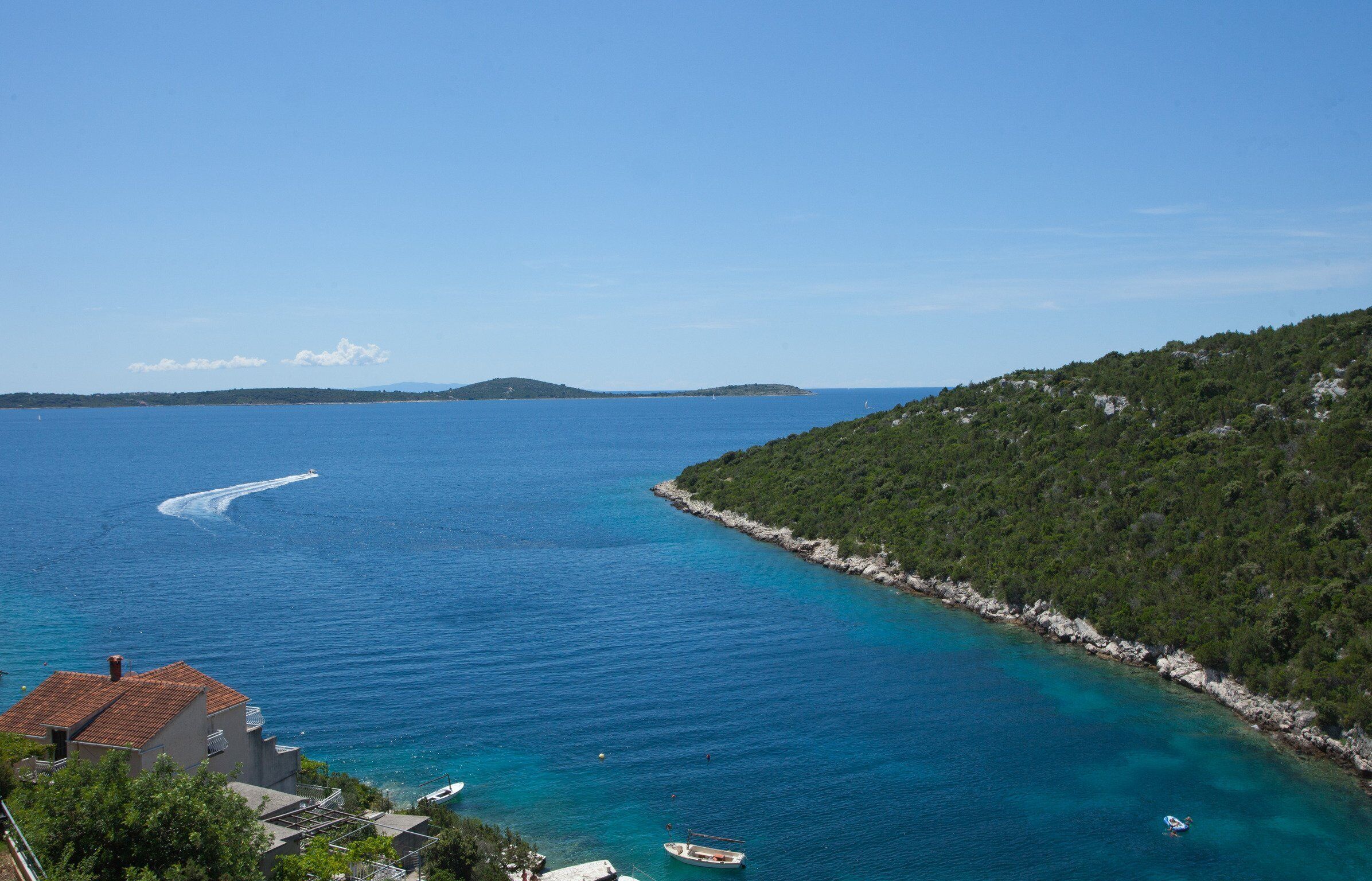 Vista costera con aguas azules cristalinas, un barco y un pequeño edificio.