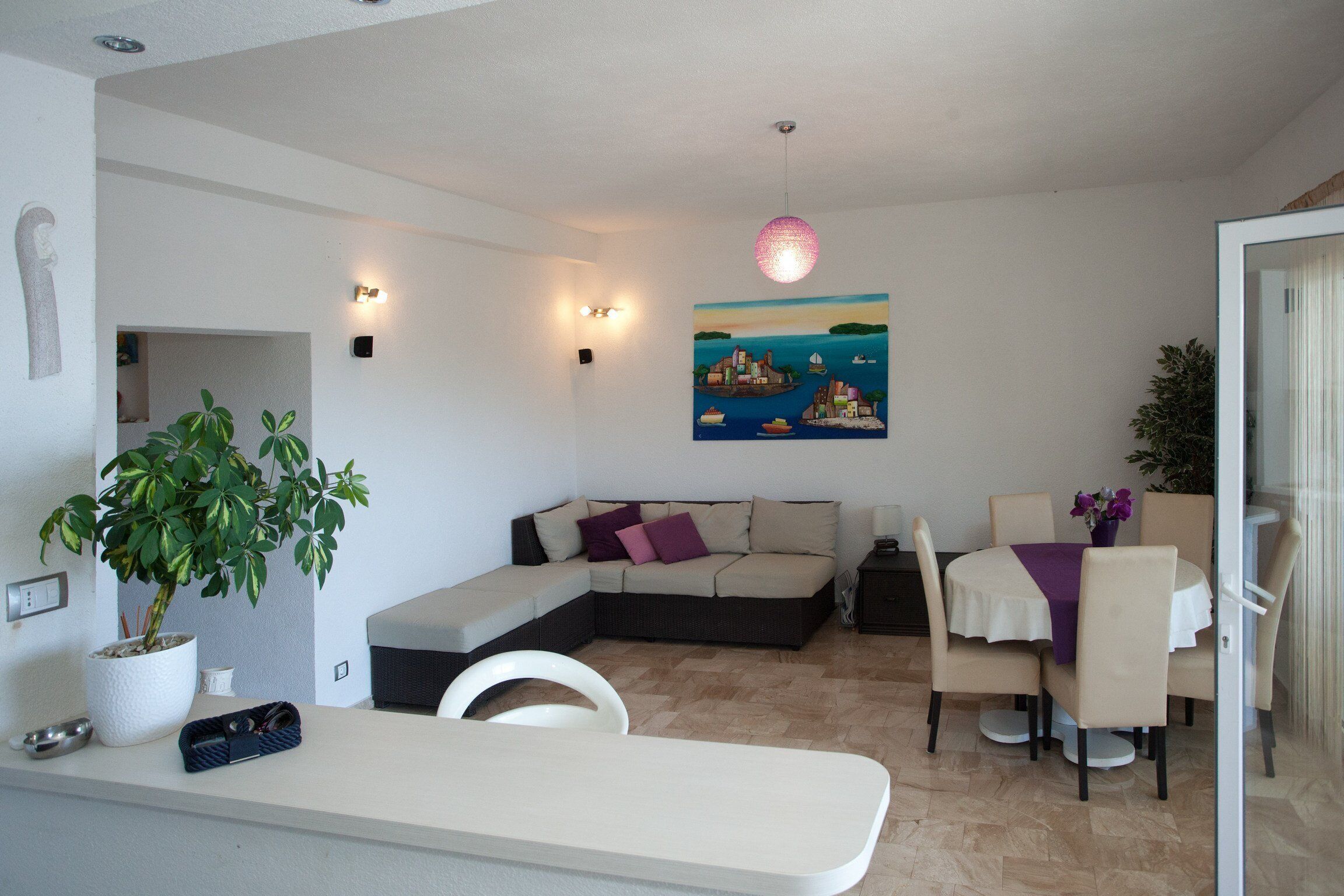 A modern living room with a sectional sofa, a dining table with chairs, a potted plant, and a painting on the wall.