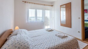 A bedroom with a bed, a window with sheer curtains, a bedside lamp, a mirror, and a door leading to another room. - Charming Trogir Apartments With Balcony (Trogir)