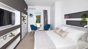 Moderni hotellihuone, jossa on suuri sänky, kaksi tuolia, televisio ja parveke, jolta on näkymä.