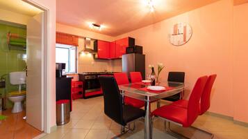 Una cocina compacta con armarios rojos, una mesa de comedor con sillas rojas y un reloj visible en la pared.