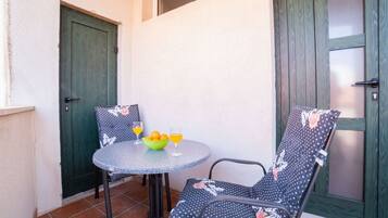 Un petit espace patio avec une table ronde et deux chaises, un saladier rempli de fruits et deux verres de jus d’orange.