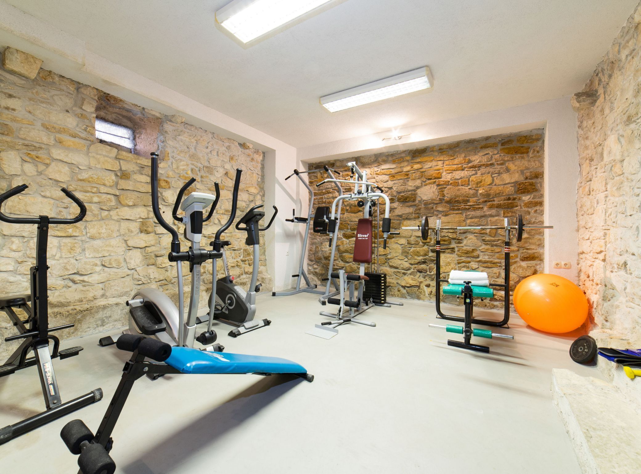 Una palestra in casa con diverse attrezzature per esercizi, tra cui una cyclette, un ellittico, una panca per pesi e una rastremazione.