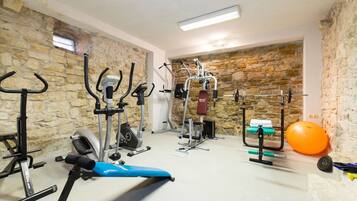 Una palestra in casa con diverse attrezzature per esercizi, tra cui una cyclette, un ellittico, una panca per pesi e una rastremazione.