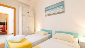 Une chambre avec deux lits, une armoire, un tableau représentant la mer, et une salle de bain visible à travers une porte ouverte.