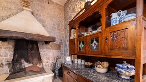 Une cuisine rustique avec un mur en pierre, un poêle à bois et un plan de travail en marbre, le tout agrémenté de meubles de rangement en bois.