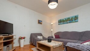 Una sala de estar moderna con una televisión de pantalla plana, un sofá gris, una mesa de centro de madera y un cuadro de palmeras.