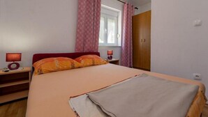 Un dormitorio con cama, dos mesitas de noche, una ventana con cortinas y un armario.