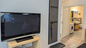 Ein modernes Wohnzimmer mit einem großen Flachbildfernseher, einer integrierten Soundbar und einer vertikalen, schwarz-weißen Streifenwand.