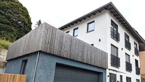Ein modernes, zweistöckiges Gebäude mit Garage, großen Fenstern und einem geneigten Dach.