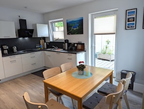 Une cuisine moderne avec des meubles blancs, une table à manger en bois et une vue sur l’extérieur.