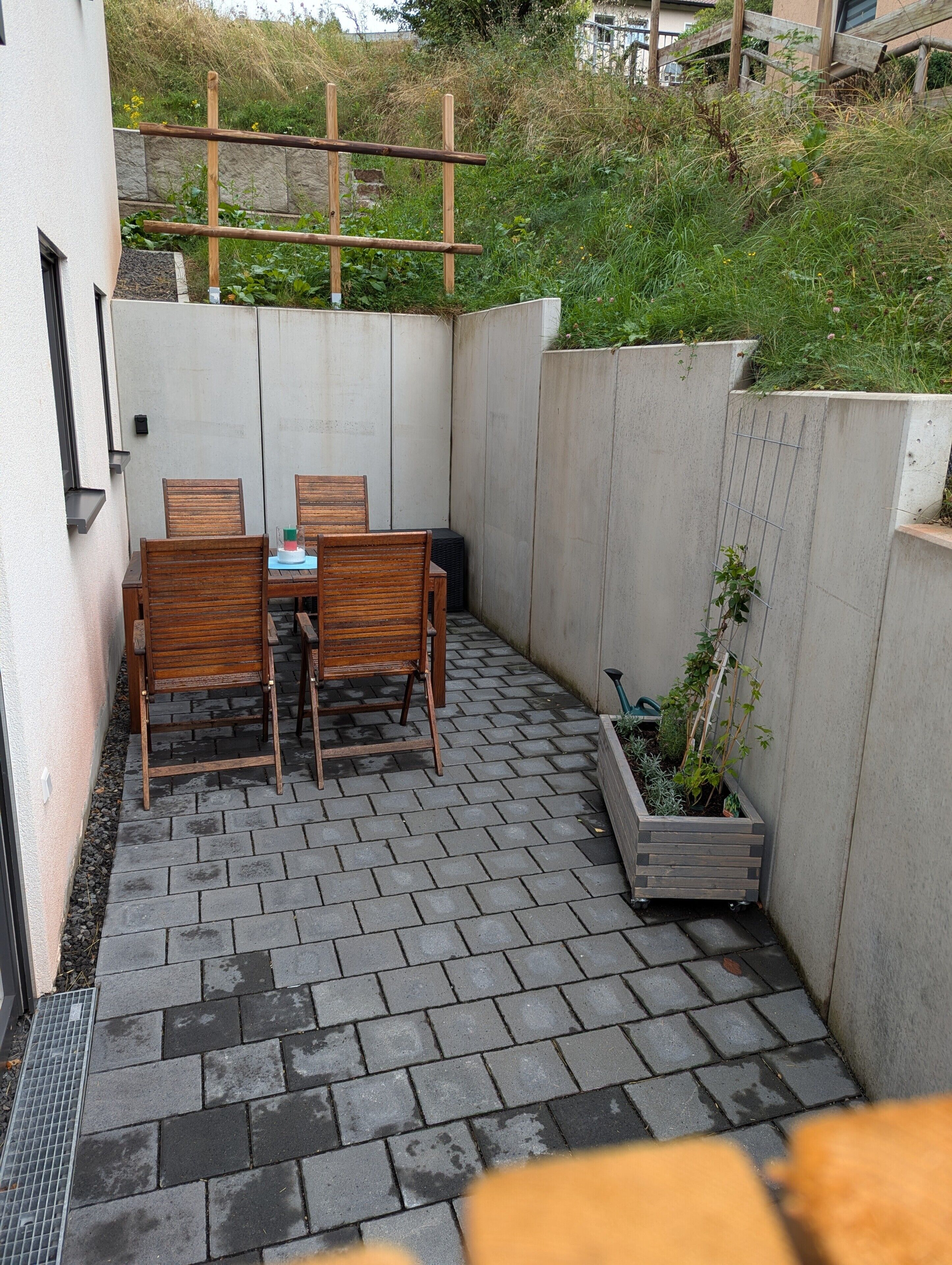 Une terrasse avec une table et des chaises, un mur en béton et une treille en bois.
