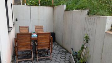 Une terrasse avec une table et des chaises, un mur en béton et une treille en bois.