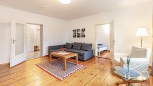Un salon avec un canapé gris, une table basse en bois, une table d’appoint en verre, un fauteuil blanc et un tapis à motifs.