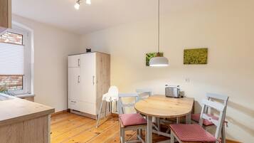 A compact kitchen with a wooden countertop, a white cabinet, a round wooden table with four chairs, a toaster, and a hanging light fixture.