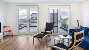 Un soggiorno moderno con un balcone, una poltrona rossa, una poltrona nera, un divano blu e un tavolino.