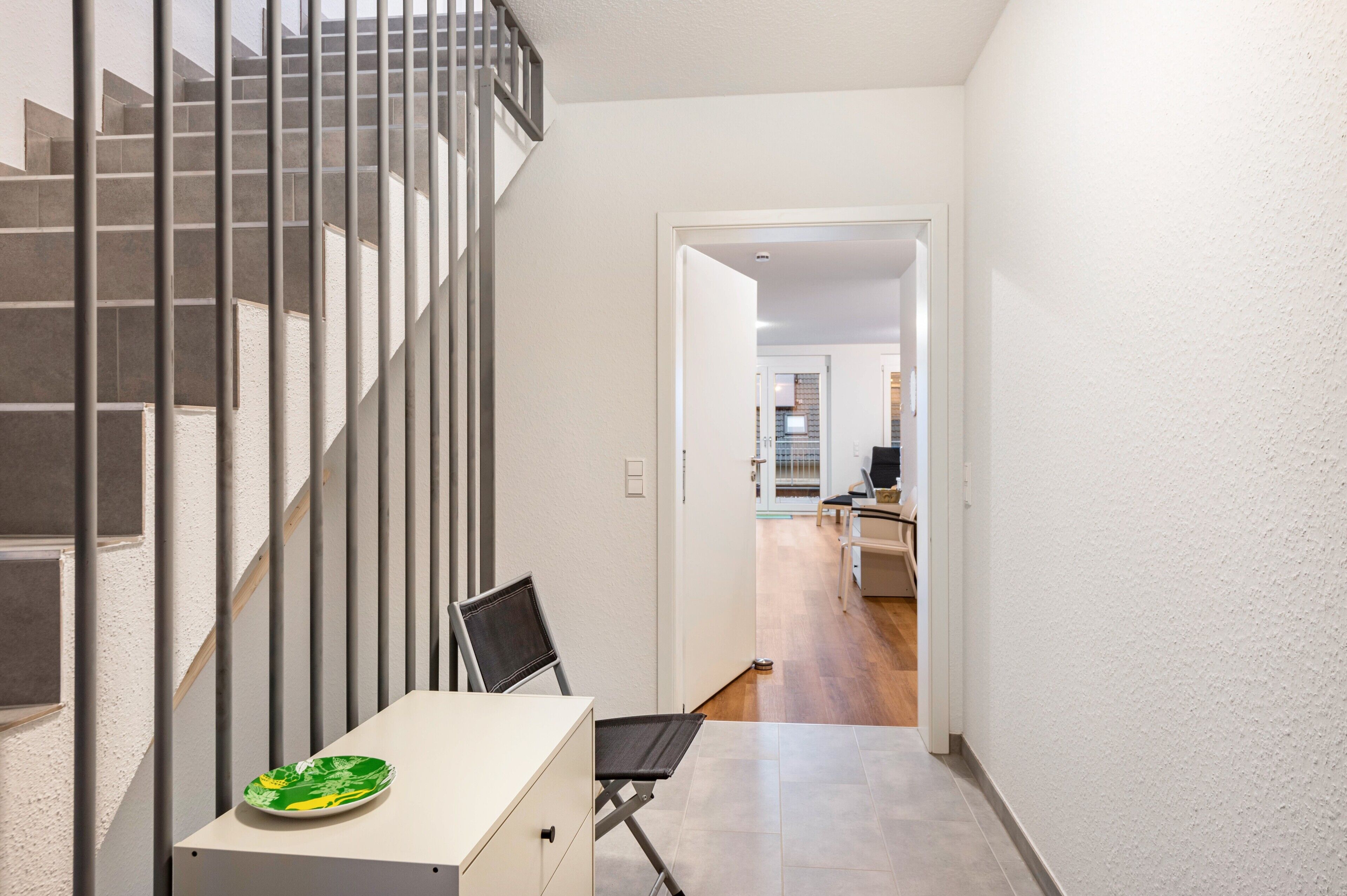 A modern interior with a staircase, a dining area with a table and chairs, and a kitchen in the background.
