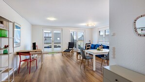 Una stanza moderna e luminosa con pavimento in legno, una scrivania con sedia, un tavolo da pranzo con sedie, un divano e un grande specchio appeso alla parete.