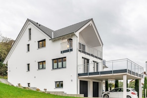 A modern two-story house with a balcony, a garage, and a car parked in front.