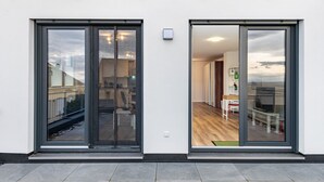 Un edificio moderno con ampie porte scorrevoli in vetro, una facciata bianca e pulita, e un interno con pavimenti e mobili in legno.