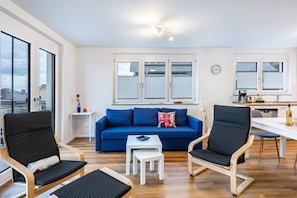 A modern living room with a sofa, chairs, a small table, and a kitchen area with a dining table.