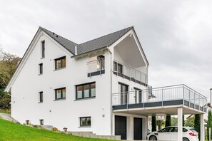 Une maison moderne à deux étages, dotée d’un balcon, d’un garage et d’une voiture garée devant.