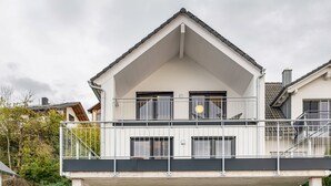 A two-story building with a balcony, a visible staircase, and a window with a circular object.