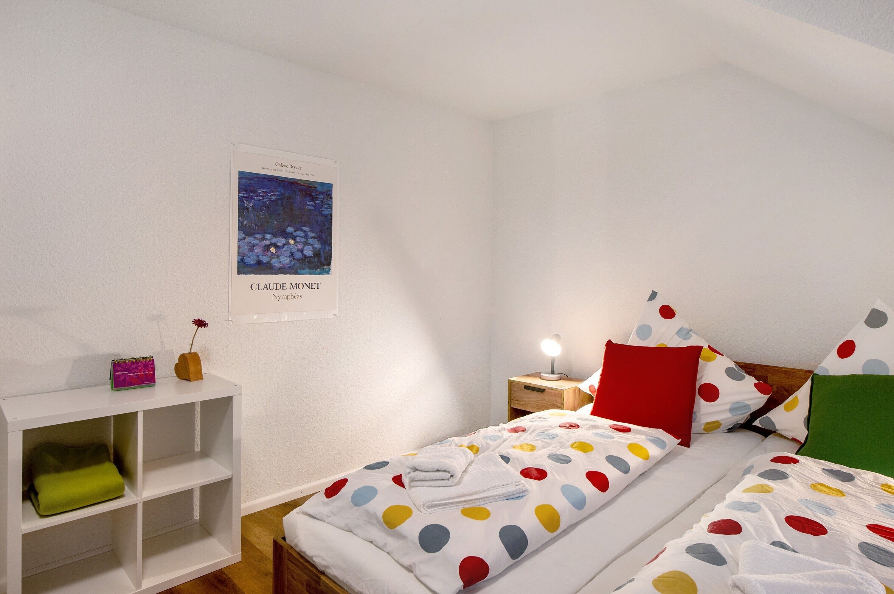 A bedroom with a bed, a nightstand, a bedside table, a shelf unit, and a poster on the wall.