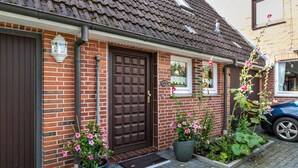 A brick house with a brown door, potted plants, and a blue car parked outside. - Apartment 'Gode Tied' with Private Terrace, Balcony and Wi-Fi (Wesseln)