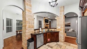A modern kitchen with stone pillars, a built-in dishwasher, and a grey sofa in the living area. - The Cove: Heated Pool, Hot Tub, Lake Access (Shady Shores)