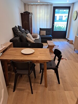 A living room with a dining table, two sofas, a wooden cabinet, and a view through a window.