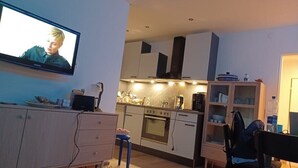 Un espace de vie compact comprenant un coin cuisine, un téléviseur fixé au mur et un coin repas avec une chaise.
