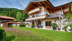Een chalet met twee verdiepingen, een balkon, een terras met tuinmeubilair en een tuin vol wilde bloemen.