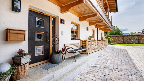 Een gebouw met een houten balkon, een zwarte deur en een bank voor buiten.
