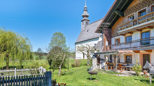 A traditional wooden house with a balcony, a stone tower, and a well-maintained garden.