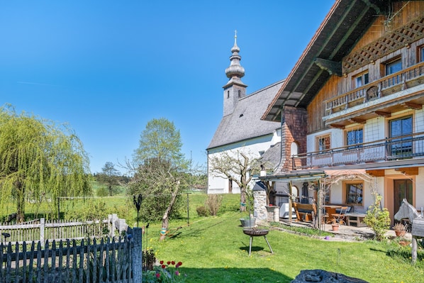 Une maison traditionnelle en bois, dotée d’un balcon, d’une tour en pierre et d’un jardin bien entretenu.