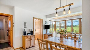 A dining area with a wooden table, chairs, a television, and a view of the outdoors.